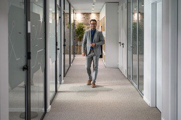 Fototapeta premium Full length of male professional in eyeglasses looking at camera while standing in office corridor