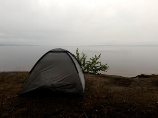 a tourist tent stands on the shore of a cliff in front of a huge sea, a traveler has set himself temporary accommodation to relax and go on a long journey to wander, tourist equipment