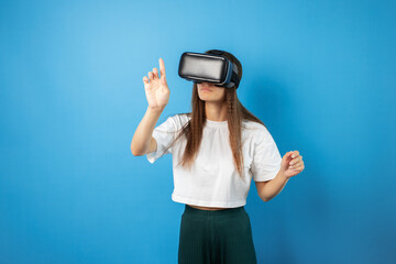 Teenage student in VR helmet, portrait of curly teen using advanced headset, young person in a studio,positive girl interacting with virtual worlds, modern technology in the blue background.