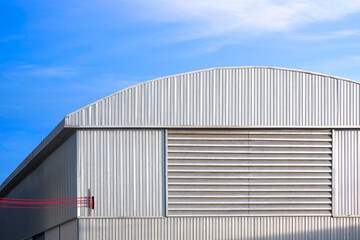 Fototapeta premium Large industrial warehouse with louver ventilation on aluminum corrugated wall with red cable lines wiring into building against blue sky background, perspective side view