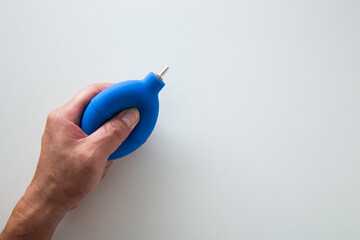 Hand is squeezing a blue air blower pump dust cleaner on a white background