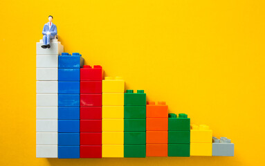 Businessman figurine sitting on top of colorful plastic toy brick graph representing business success and career progress