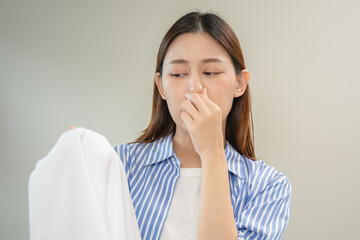 housewife smelling bad odor from damp clothes during laundry.