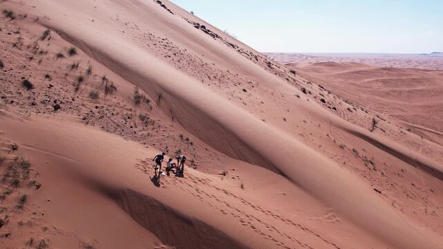 Drone view of people riding on a board on the sand dunes of the desert