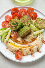 Hummus served with paprika, falafel, fresh tomatoes and cucumber on a white plate, middle close-up, vertical shot, selective focus