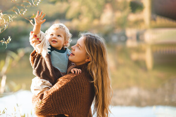 Smiling happy young mother 24-26 year old holding baby girl over lake and nature background. Autumn...