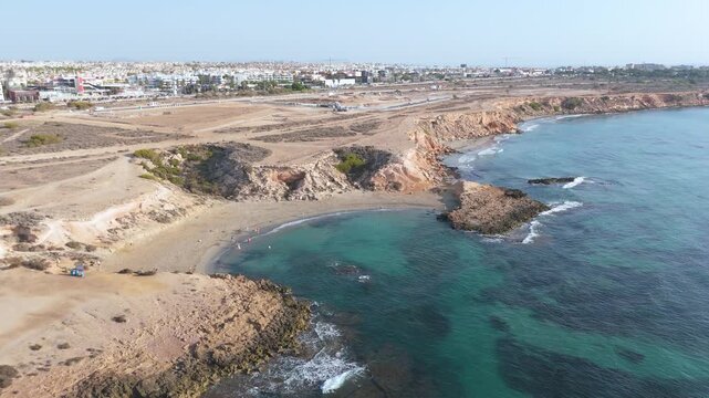 Drone flies over Playa Flamenca, capturing a comprehensive aerial view of the dog beach, rugged coastline, and urban landscape of Orihuela, Costa Blanca, Spain.