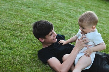 An older brother and a small child in a diaper are playing with a ball on the green grass in the yard