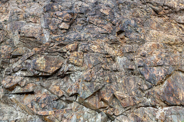 Rock background. Brown stone texture. Mountain surface close-up. Distressed, cracked, collapsed, crumbled, broken. Rough rock wall, natural stone background texture. Volcanic rock with rust inclusions