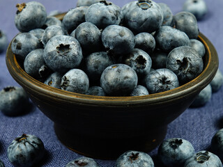 Brown ceramic bowl filled with ripe fresh blueberries stands on dark blue fabric