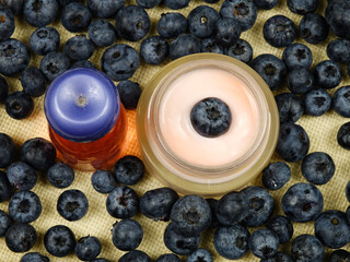 Bottle and jar with beauty products based on a blueberry extract, ripe fresh blueberries are on a table