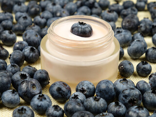 Jar with beauty product based on a blueberry extract, ripe fresh blueberries are on a table