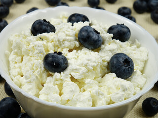     Fresh cottage cheese with blueberries is in a white bowl on the table, healthy food with cottage cheese and berries    