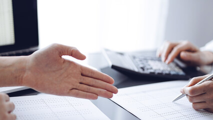 Woman accountant using a calculator and laptop computer while counting and discussing taxes with a client. Business audit concepts