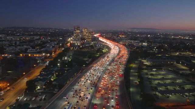 Gazing down, witness a densely packed traffic scenario in downtown Los Angeles, blending in beautifully with the twilight sky. The cars lights create a lively glow amid the urban landscape