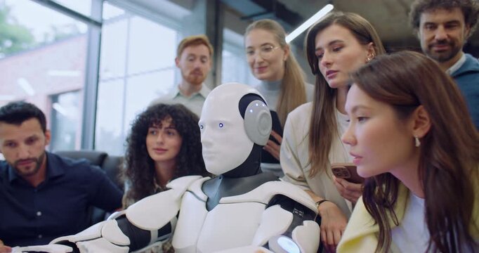 Multi-ethnic group of people surrounding robot. Giving command to press specific key on keyboard in front of gadget. Bionic person complies and performs request correctly. Team happy about success.