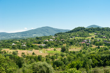 Fototapeta premium A village drowning in green gardens in the middle of a mountain landscape against the background of a clear blue sky