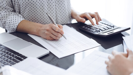 Woman accountant using a calculator and laptop computer while counting taxes for a client. Business...