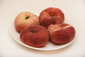 Flat peaches on a white plate. Delicious yellow peaches.
