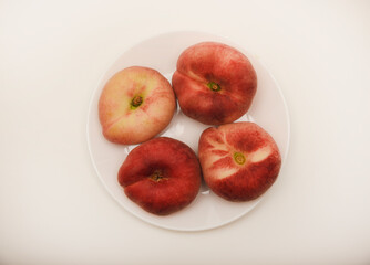 Flat peaches on a white plate. Delicious yellow peaches.