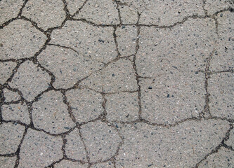 The asphalt is cracked from time and wear. The texture of the road surface has wet cracks.