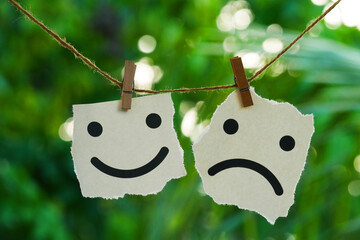 two pieces of paper with symbols of a smiley face and a sad face hanging on a rope with a natural...