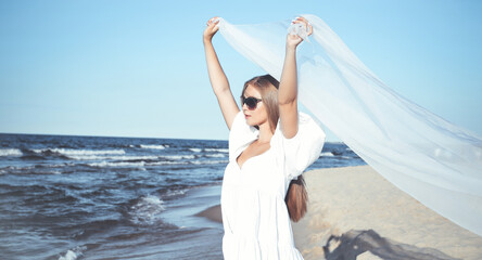 Happy blonde woman is catching clouds and wind with her arms on the ocean beach