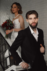 Groom man in Black Suit Posing with Bride Holding Red Bouquet in Background.