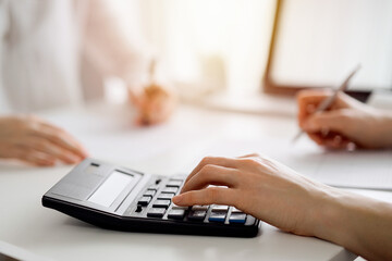 Two accountants using a calculator and laptop computer for counting taxes at white desk in office. Teamwork in business audit and finance