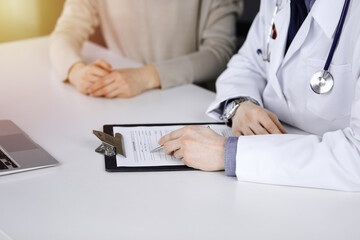 Unknown male doctor and patient woman discussing something while sittingin a darkened clinic and...