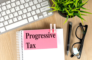 PROGRESSIVE TAX text pink sticky on notebook with keyboard, pen and glasses