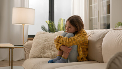 Bored disappointed little Caucasian girl schoolgirl daughter kid hug knees alone home thinking...