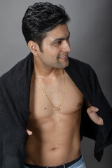 Cropped view of a young shirtless athlete with black towel after shower, bath or sauna. Indian bodybuilder with happy, mischievous facial expressions posing for camera