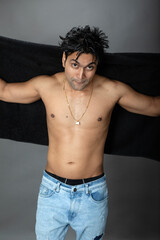 Naklejka premium Cropped view of a young shirtless athlete with black towel after shower, bath or sauna. Indian bodybuilder with happy, mischievous facial expressions posing for camera