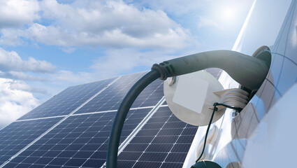 Close up of electric car with a connected charging cable on the background of solar panels. © scharfsinn86