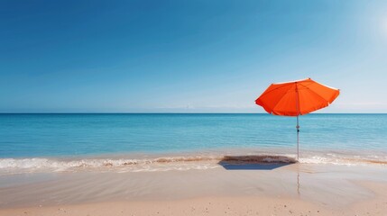 Fototapeta premium Orange Umbrella on Sandy Beach by the Calm Ocean Under Clear Sky
