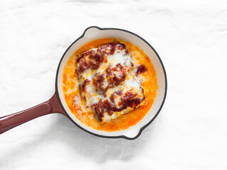 Zucchini cannelloni stuffed with minced meat and bulgur, baked with tomato sauce and mozzarella in a frying pan on a light background