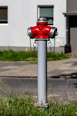A red and silver fire hydrant located on a gray pole in front of a white building. The fire hydrant...