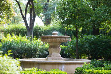 Stone fountain surrounded by green vegetation in a park in Seville, Spain.