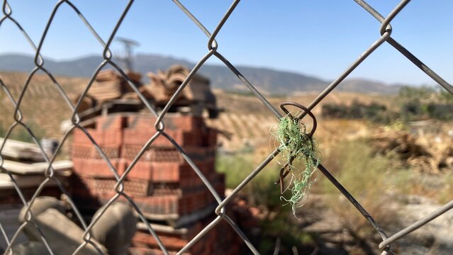 Parcela exterior vallada con restos de materiales para la construcci&oacute;n como ladrillos. Cielo azul y d&iacute;a soleado