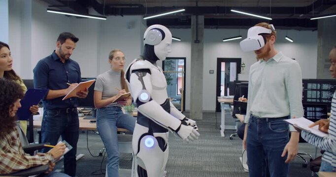 Hard working multi-ethnic team of engineers and programmers working together over some mistakes. Checking for issues with humanoid robot. Male with VR glasses trying to operate cyborg without success.