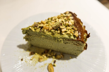 top shot close up of green pistachio basque cheese cake with nuts on top on a white plate