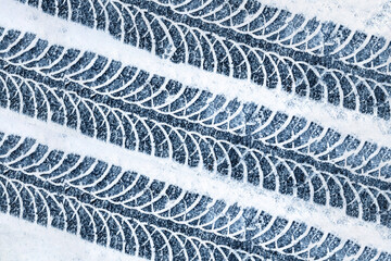 Snow tyre mark. Asphalt covered in snow. Dangerous road conditions. Car imprint on frozen ground. Tire trail on ice. City streets covered in snow during heavy snow fall. Slippery road background.