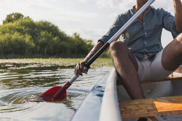 Young man canoeing, paddling, and moving canoe through the lake water, enjoying the natural...
