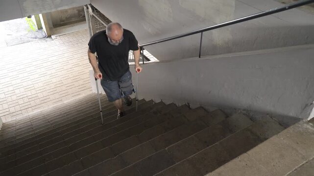 Mature man with bondage, medical splint, knee brace on the leg climbing the stairs using crutches. Accessible urban environment for the disabled, recovery from injury. Adaptation of people with