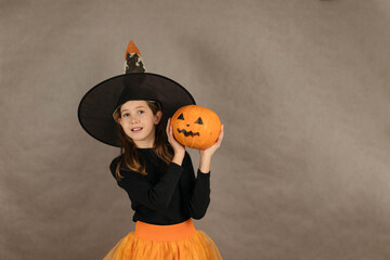 close up portrait of a teenage girl in a witch costume with a pumpkin for Halloween in her hands on...
