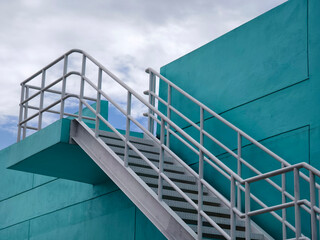 Metal stairs to blue building against sky and clouds