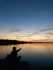 Sunset lake view and a silhouette man with a hat