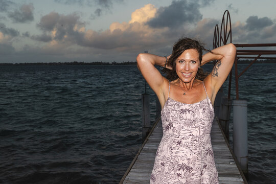 Pretty middle aged woman standing on a dock outside over the south pacific ocean on the tropical island Bora Bora. She is on vacation with a deep tan, smiling, and it is dark outside. 