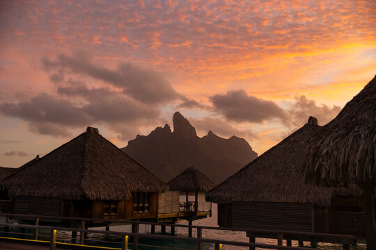 Vibrant red and orange sunset over Mount Otemanu on the tropical island of Bora Bora. Overwater bungalow huts have a perfect view of the natural scenery. 